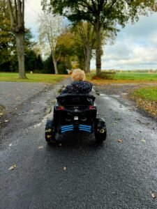 Foto in kleur van dreumes in een elektrische kinderauto op de straat