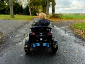 Foto in kleur van dreumes in een elektrische kinderauto op de straat