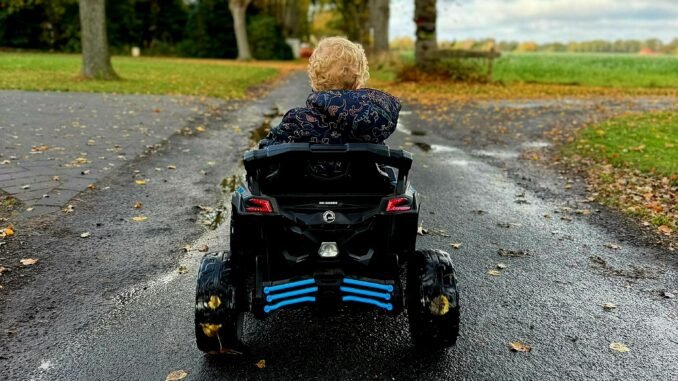 Foto in kleur van dreumes in een elektrische kinderauto op de straat